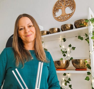 Chrissy holding a pair of tuning forks with Himalayan singing bowls on a shelf in the background