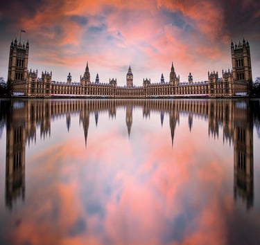 A wide reflection of the Palace of Westminster and Big Ben in London under a vibrant orange sunset sky.