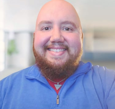 Smiling bald man with a red beard wearing a blue quarter-zip pullover and a silver necklace.