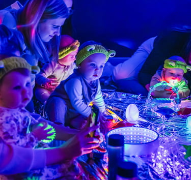 Babies in baby moo playing with the lights turned off and glow up instruments for space week,