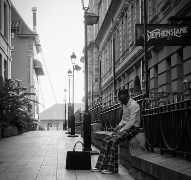 A man in plaid trousers sits on a stone ledge in a black and white urban alleyway near Stephens Lane.