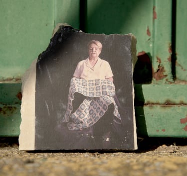Vintage portrait of a seated woman holding a quilt, printed on a stone shard against a green door.