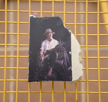 A torn vintage photo of a man in a straw hat with a dog resting on a yellow grid surface.