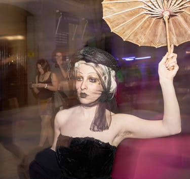 Woman in vintage gothic costume with a black veil, gold makeup, and holding a tan parasol.