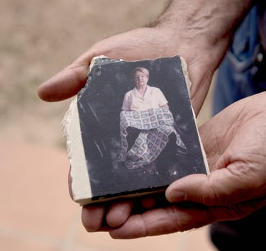 Hands holding a broken ceramic tile featuring a portrait of an elderly woman holding a blanket.