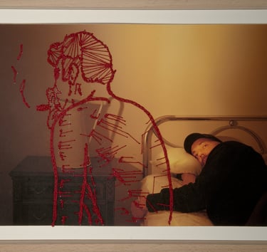 Red embroidery of a figure overlaying a photograph of a man lying in a metal bed frame.