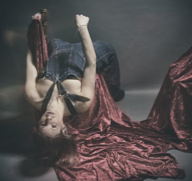 Artistic portrait of a woman in denim overalls posing upside down on red velvet fabric.