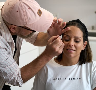 Professional makeup artist applying eyebrow liner and eyeshadow to a woman in a bright studio.
