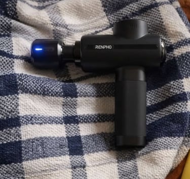 Handheld massage gun resting on a blanket for muscle recovery and relaxation