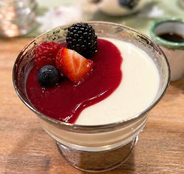 Creamy vanilla panna cotta dessert topped with red berry coulis and fresh mixed berries in a glass bowl.