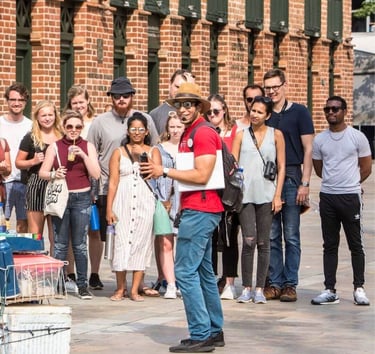 A tour guide in a red shirt leads a walking tour group in front of a historic brick building.