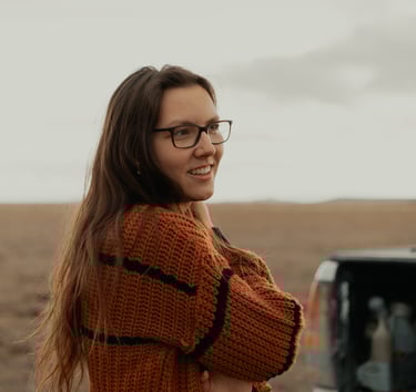 a woman in glasses and a sweater standing in front of a truck
