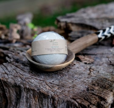 a light green round bath bomb on a wooden spoon on a tree stump