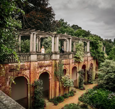 Bride and groom standing on a terrace of a historic brick building surrounded by greenery
