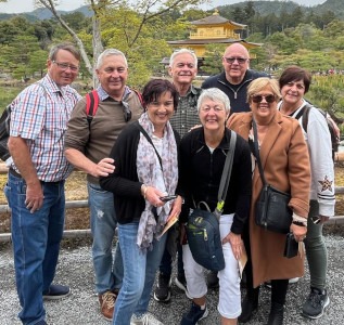 Group of eight people with trees and a traditional Japanese building in the background.