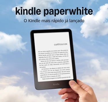 A person holding an Amazon Kindle Paperwhite e-reader displaying a book in Portuguese against a blue sky with clouds.
