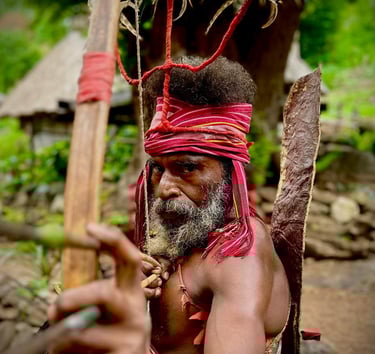 Indigenous hunter from Alor Island, Indonesia, wearing a feather headdress and aiming a traditional bow.