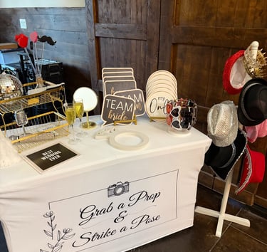 Wedding photo booth prop station with signs, hats, and glasses on a white table.