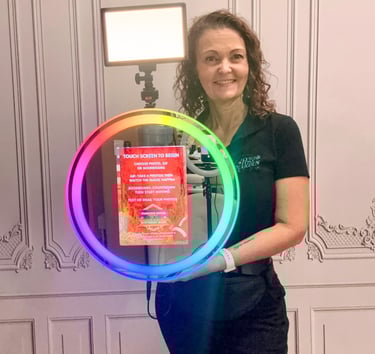 A woman holding a portable ring light photo booth with rainbow LED lighting for events.
