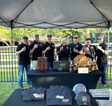 Bullets & Bourbon members standing together holding glasses of bourbon behind a table of different bourbon bottles