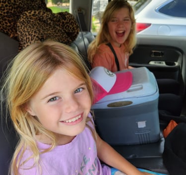 Mary Grace and Cecelia smiling in the backseat of a car .