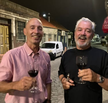two men standing next to each other holding wine glasses