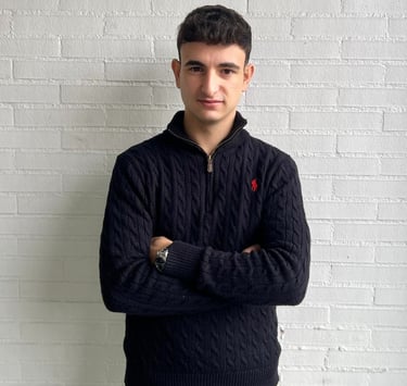 a man in a sweater and jeans standing in front of a white brick wall