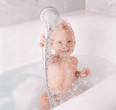 Happy baby playing in a safe clean shower bath after professional repairs in an Auckland home