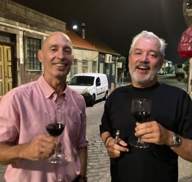 two men standing next to each other holding wine glasses