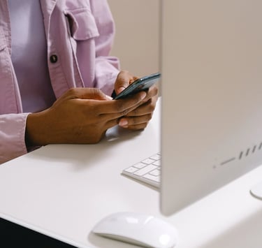 Femme brune, assise à son bureau, qui pianote sur son téléphone portable devant son ordinateur