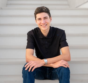 A stylish, confident young entrepreneur poses on stairs with direct eye contact and a welcoming smile.