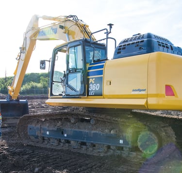 A heavy equipment technician is seen approaching a Komatsu PC360LCi smart construction excavator.