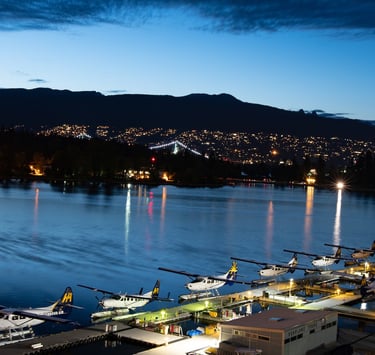 Harbour Air float aircraft lined up at Vancouver's dock at night, with Stanley Park and the Lions Gate bridge illuminated.