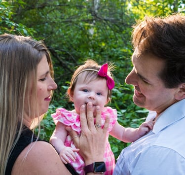 A happy couple holding the child and gazing at her. The child glances at the camera, smiling slightly. 