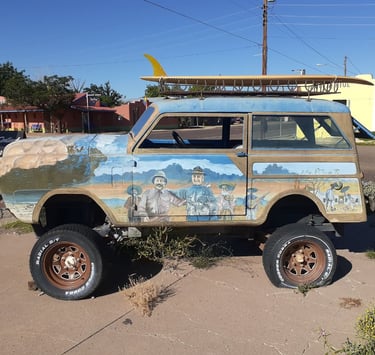 Broken-down sand buggy parked with a surfboard strapped on top.
