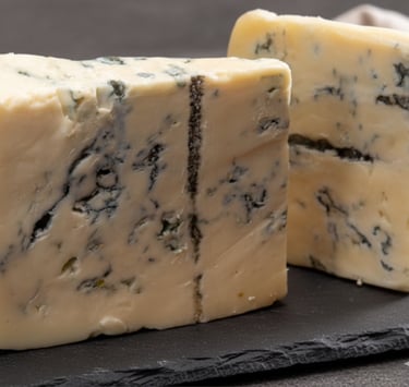 Two thick wedges of creamy blue cheese with blue-green veins on a black slate serving board.