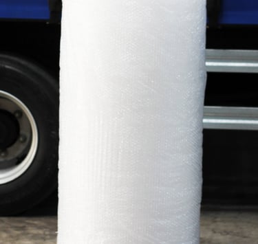 Rolo de plástico bolha grande, ao fundo um caminhão de entregas.