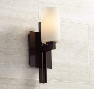 Modern dark bronze wall sconce with a cylindrical white frosted glass shade mounted on a tiled wall.