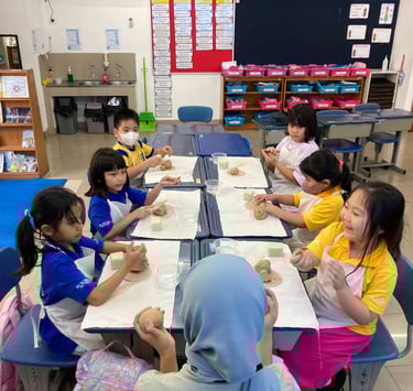 a group of children sitting at a table and making pottery together