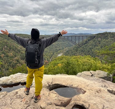 Person with outstretched arms enjoying the view at New River Gorge, West Virginia, surrounded by mou