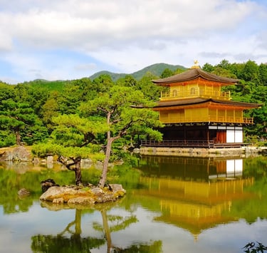 Golden Pavilion Kinkaku-ji temple in Kyoto reflected in a Zen garden pond with lush trees.