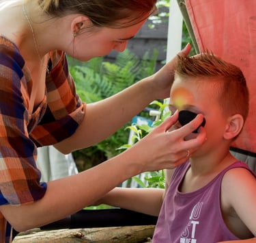 Een jongetje krijgt geconcentreerd een stoer oogmasker geschminkt met een sponsje.