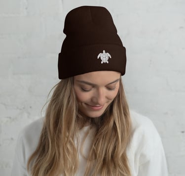 A woman wearing a dark brown cuffed beanie with a white sea turtle embroidery.