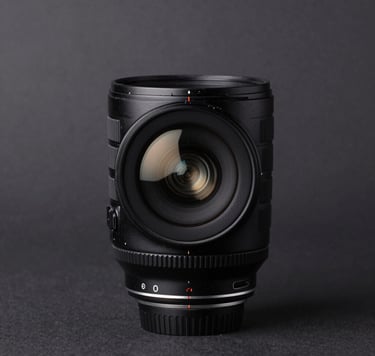 A minimalist studio shot of a professional camera lens on a dark surface. The focus is on the subtle off-white light reflecting off the glass elements. Clean, sophisticated composition set in a North American / US photography studio.
