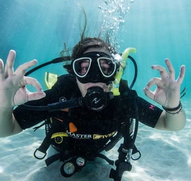 A scuba diver underwater gives the OK hand sign while wearing professional diving gear and a mask.