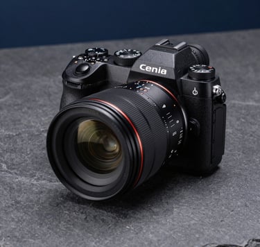 A sharp, detailed photograph of a professional mirrorless camera with a large aperture lens, resting on a charcoal gray textured surface. The lighting is dramatic yet clean, highlighting the precision dials and glass optics, set in a modern North American studio environment with cool slate and dark blue tones.