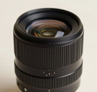 Minimalist macro photography of a photography lens reflecting soft, ambient light in a studio setting. The composition is artistic and high-end, with deep shadows and soft highlights of #FDFBF7. Elegant and professional atmosphere.