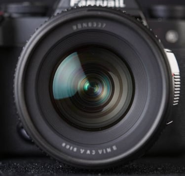 A macro photograph of professional camera equipment, focusing on the precision-engineered glass of a lens reflecting soft pale steel blue light against a deep rich obsidian background.