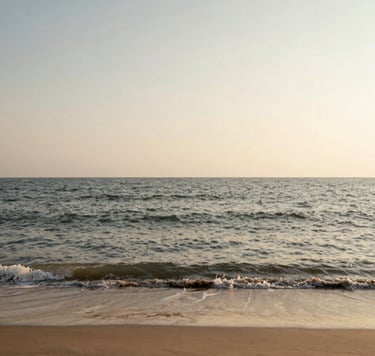 An evocative landscape photo of a tranquil beach at dawn. The sand is a Warm Sandy Taupe, and the gentle waves are a mix of Charcoal Olive and Muted Earth Brown reflections. The sky is a vast, serene Soft Creamy Off-White, reflecting a soulful and powerful connection to nature.
