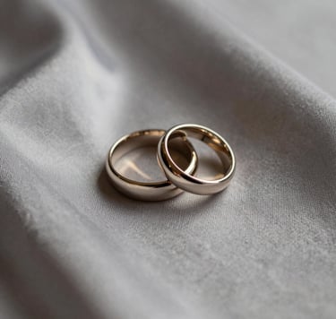 Detailed photography of a pair of high-end wedding rings resting on a warm grey silk fabric, soft morning light, minimalist and sophisticated composition, cream and taupe tones, Hispanic setting.